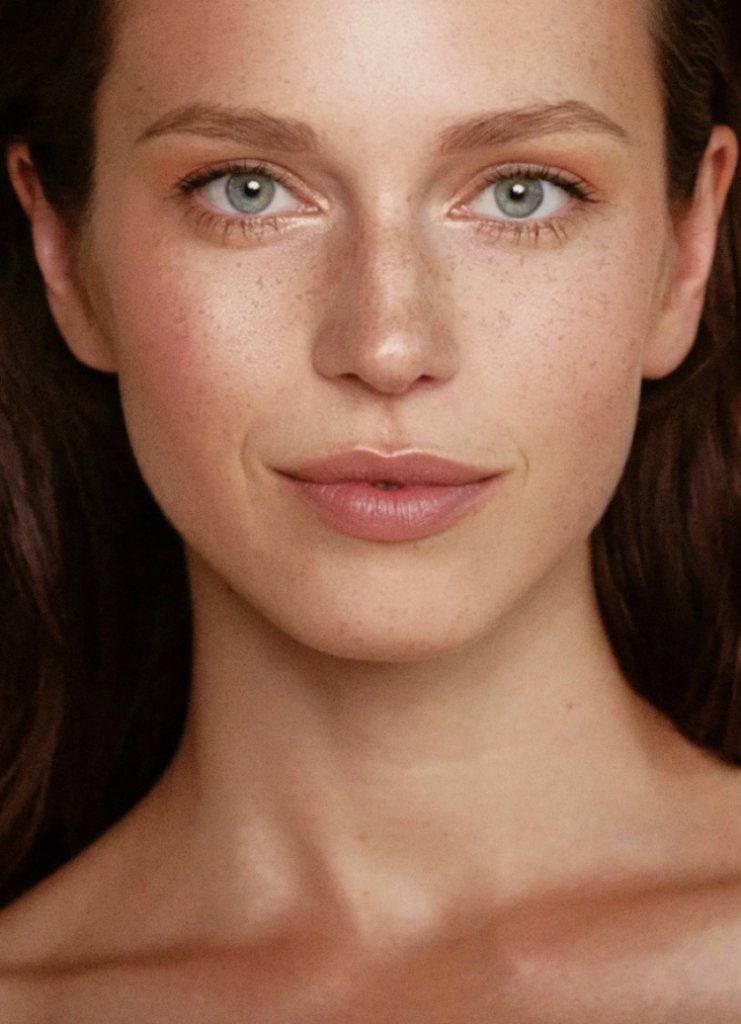 Woman with clear, freckled skin smiles at camera