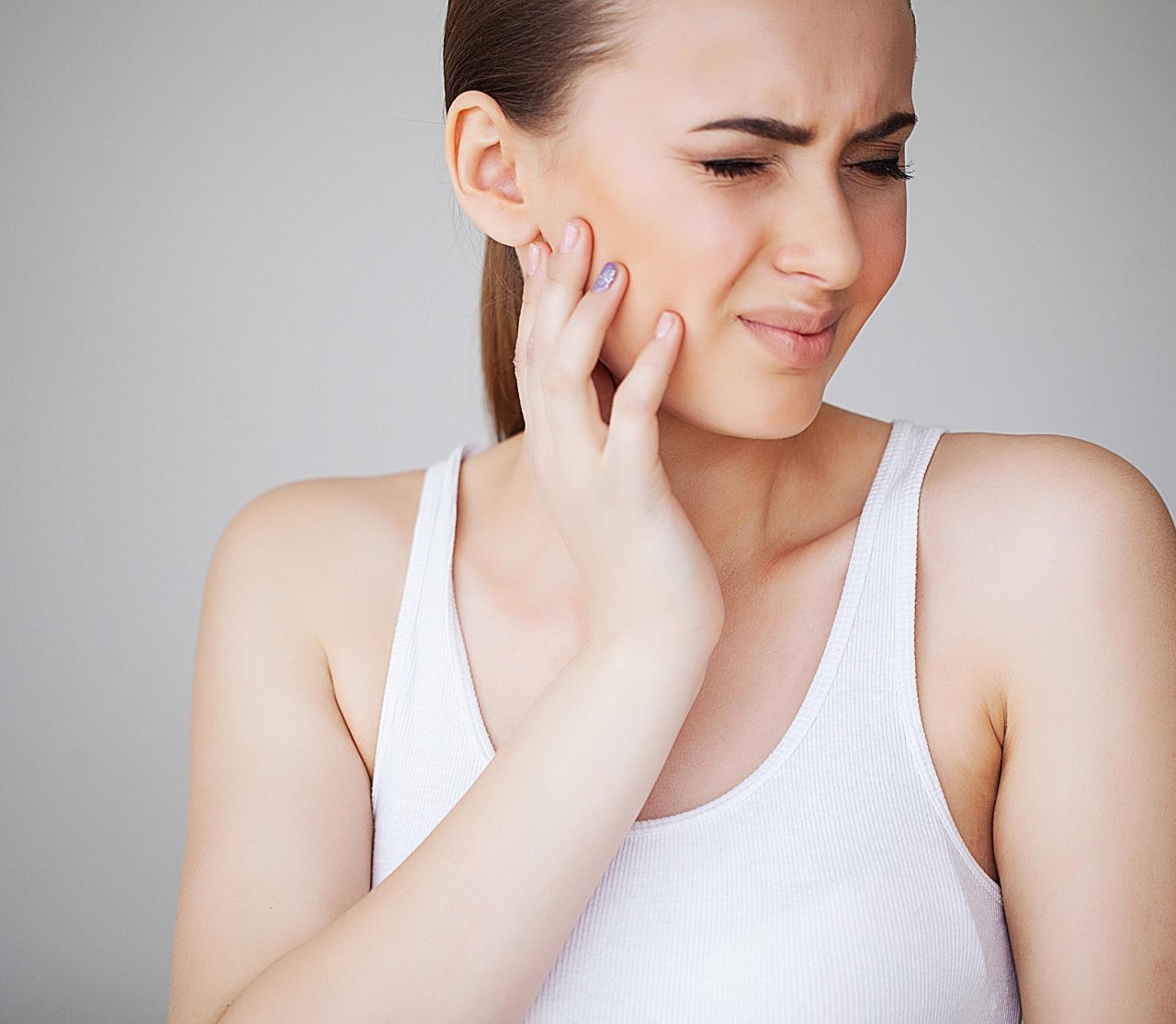 Woman experiencing jaw pain, holding jaw in pain and grimacing